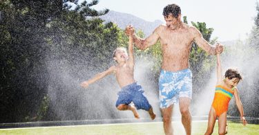 family playing in sprinkler in summer