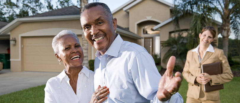 elderly couple standing in front of realtor and house